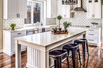 Design ideas for a mid-sized country u-shaped kitchen in Detroit with a farmhouse sink, recessed-panel cabinets, yellow cabinets, quartz benchtops, white splashback, ceramic splashback, stainless steel appliances, medium hardwood floors, with island, brown floor and yellow benchtop.