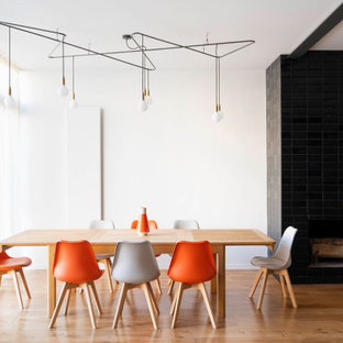 Exemple d'une grande salle à manger ouverte sur le salon tendance avec un mur blanc, un sol en bois brun, une cheminée standard, un manteau de cheminée en carrelage et un sol beige.