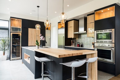 Example of a mid-sized trendy l-shaped ceramic tile and gray floor kitchen design in Montreal with an undermount sink, flat-panel cabinets, black cabinets, quartz countertops, gray backsplash, ceramic backsplash, stainless steel appliances and an island