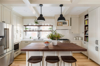 Foto på ett avskilt, mellanstort vintage vit u-kök, med en undermonterad diskho, luckor med infälld panel, vita skåp, bänkskiva i kvarts, vitt stänkskydd, stänkskydd i keramik, rostfria vitvaror, ljust trägolv, en köksö och brunt golv