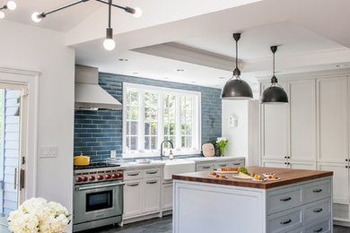 This is an example of a large transitional l-shaped kitchen in New York with a farmhouse sink, shaker cabinets, white cabinets, wood benchtops, blue splashback, subway tile splashback, stainless steel appliances, porcelain floors, with island and brown floor.
