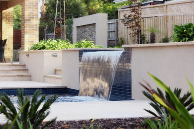 This is an example of a large beach style backyard rectangular pool in Sydney with a water feature and natural stone pavers.