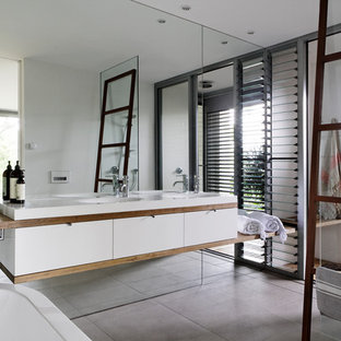 Aménagement d'une salle de bain principale contemporaine de taille moyenne avec un placard à porte affleurante, des portes de placard en bois brun, une baignoire indépendante, une douche ouverte, un WC suspendu, des carreaux de miroir, un sol en carrelage de porcelaine, un lavabo intégré, un plan de toilette en bois, un sol gris, aucune cabine et un plan de toilette blanc.