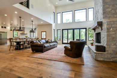 Example of a large arts and crafts open concept dark wood floor and vaulted ceiling living room design in New York with white walls, a standard fireplace, a stone fireplace and a wall-mounted tv