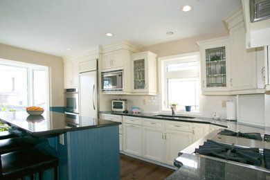 Inspiration for a mid-sized farmhouse l-shaped medium tone wood floor eat-in kitchen remodel in Other with a double-bowl sink, recessed-panel cabinets, white cabinets, white backsplash, subway tile backsplash, white appliances, an island and granite countertops