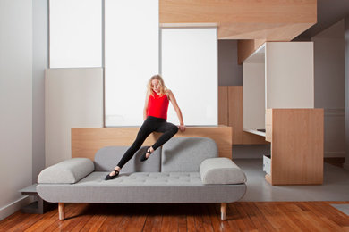 Modelo de sala de estar abierta actual de tamaño medio sin chimenea y televisor con paredes grises, suelo de madera clara, suelo marrón y madera