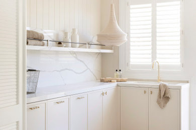 Large country laundry room in Sydney with beige cabinets, marble benchtops, white splashback, marble splashback, beige walls, ceramic floors, a side-by-side washer and dryer, multi-coloured floor, white benchtop and panelled walls.