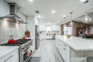 Photo of a large classic l-shaped kitchen/diner in Houston with a belfast sink, shaker cabinets, white cabinets, quartz worktops, white splashback, ceramic splashback, stainless steel appliances, porcelain flooring, an island, beige floors, white worktops and a coffered ceiling.