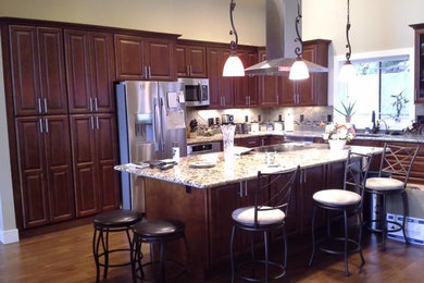Example of a large l-shaped medium tone wood floor open concept kitchen design in Portland with a double-bowl sink, dark wood cabinets, granite countertops, beige backsplash, ceramic backsplash, stainless steel appliances and an island