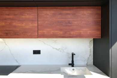 Example of a mid-sized trendy single-wall ceramic tile open concept kitchen design in Barcelona with a single-bowl sink, flat-panel cabinets, black cabinets, solid surface countertops, white backsplash, stainless steel appliances and white countertops