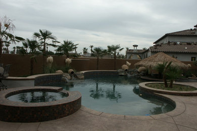 Hot tub - mid-sized tropical backyard stamped concrete and custom-shaped natural hot tub idea in Other