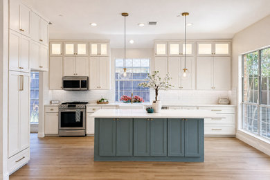Example of a large transitional l-shaped vinyl floor and brown floor open concept kitchen design in Dallas with a farmhouse sink, shaker cabinets, white cabinets, quartzite countertops, white backsplash, porcelain backsplash, stainless steel appliances, an island and white countertops