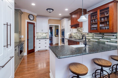 This is an example of a mid-sized transitional l-shaped eat-in kitchen in Atlanta with a farmhouse sink, shaker cabinets, white cabinets, quartz benchtops, green splashback, glass tile splashback, stainless steel appliances, medium hardwood floors and a peninsula.