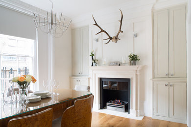 Photo of a mid-sized transitional dining room in London with grey walls, light hardwood floors, a standard fireplace and a stone fireplace surround.