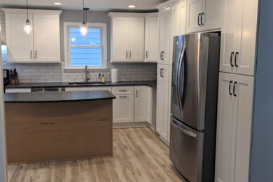 Inspiration for a small country l-shaped eat-in kitchen in Cleveland with an undermount sink, shaker cabinets, light wood cabinets, granite benchtops, white splashback, subway tile splashback, stainless steel appliances, light hardwood floors, with island and black benchtop.