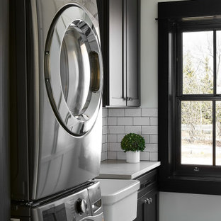 オーランドの小さいトランジショナルスタイルのおしゃれな洗濯室 (エプロンフロントシンク、シェーカースタイル扉のキャビネット、黒いキャビネット、人工大理石カウンター、白い壁、上下配置の洗濯機・乾燥機、マルチカラーの床、白いキッチンカウンター) の写真