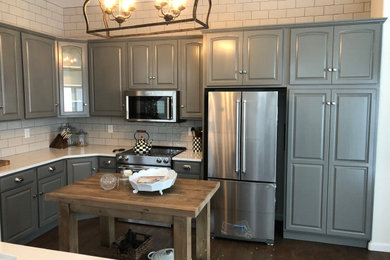 This is an example of a mid-sized transitional l-shaped kitchen pantry in Denver with raised-panel cabinets, grey cabinets, quartzite benchtops, white splashback, stainless steel appliances, dark hardwood floors, no island, brown floor and white benchtop.