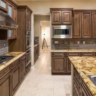 Mid-sized transitional kitchen pantry pictures - Example of a mid-sized transitional l-shaped ceramic floor kitchen pantry design in Las Vegas with a double-bowl sink, raised-panel cabinets, brown cabinets, granite countertops, gray backsplash, glass tile backsplash, stainless steel appliances and an island