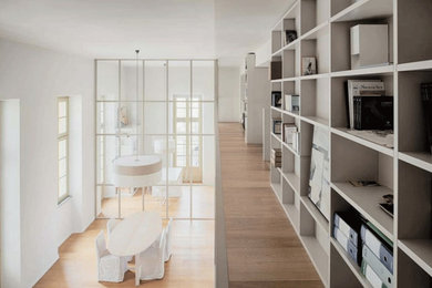 Modelo de sala de estar con biblioteca tipo loft minimalista de tamaño medio con paredes beige, suelo de madera clara, pared multimedia y suelo marrón