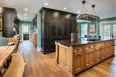 Inspiration for an expansive country eat-in kitchen in Philadelphia with an undermount sink, beaded inset cabinets, black cabinets, panelled appliances, medium hardwood floors, with island and black benchtop.