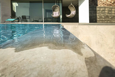 Modelo de piscina con fuente infinita minimalista de tamaño medio a medida en patio con adoquines de piedra natural