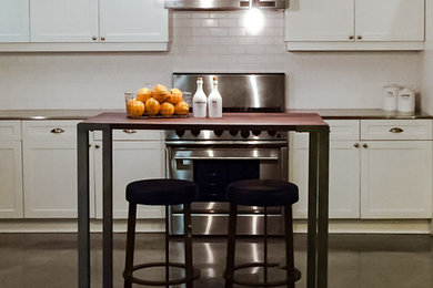 Example of a mid-sized transitional l-shaped concrete floor eat-in kitchen design in Los Angeles with recessed-panel cabinets, white cabinets, stainless steel countertops, white backsplash, subway tile backsplash, stainless steel appliances, an island and a drop-in sink