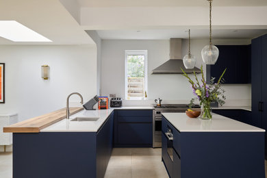 Photo of a large modern u-shaped open plan kitchen in London with a submerged sink, flat-panel cabinets, blue cabinets, engineered stone countertops, white splashback, glass sheet splashback, stainless steel appliances, an island and white worktops.