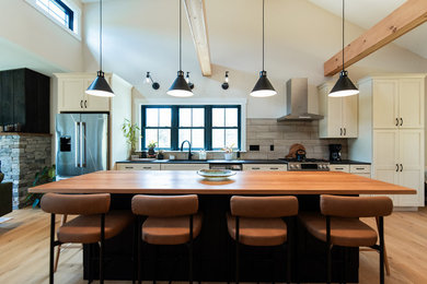 Eat-in kitchen - large farmhouse medium tone wood floor eat-in kitchen idea in Portland Maine with an undermount sink, recessed-panel cabinets, white cabinets, quartzite countertops, beige backsplash, porcelain backsplash, stainless steel appliances, an island and black countertops