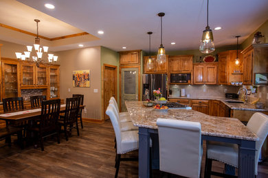 This is an example of a transitional eat-in kitchen in Kansas City with raised-panel cabinets, medium wood cabinets, granite benchtops, beige splashback, ceramic splashback, stainless steel appliances, vinyl floors, with island, brown floor and multi-coloured benchtop.