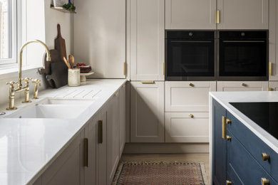 Design ideas for a large traditional grey and white kitchen/diner in London with shaker cabinets, grey cabinets, laminate countertops, white splashback, cement tile splashback, light hardwood flooring, an island, brown floors and white worktops.