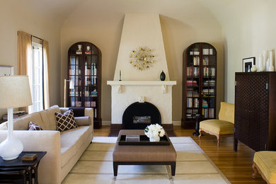 Photo of a mid-sized transitional enclosed living room in Los Angeles with beige walls, light hardwood floors, a standard fireplace, a plaster fireplace surround, no tv and brown floor.