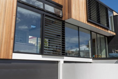 This is an example of a large modern three-storey black exterior in Auckland with wood siding and a flat roof.