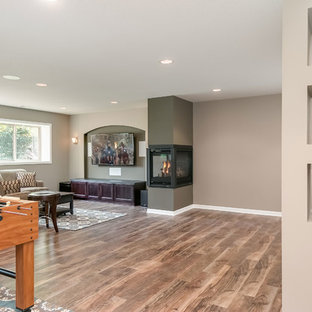 Design ideas for a medium sized traditional look-out basement in Minneapolis with beige walls, medium hardwood flooring, a two-sided fireplace, a plastered fireplace surround and brown floors.