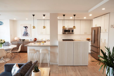 Example of a medium tone wood floor kitchen design in New York with an undermount sink, flat-panel cabinets, white cabinets, white backsplash, stainless steel appliances, an island and gray countertops
