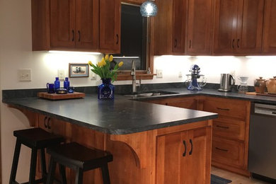 Mid-sized traditional u-shaped separate kitchen in Minneapolis with an undermount sink, recessed-panel cabinets, medium wood cabinets, granite benchtops, black splashback, stone slab splashback, stainless steel appliances, light hardwood floors, a peninsula, black benchtop and beige floor.