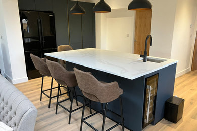 Photo of an open plan kitchen in West Midlands with a built-in sink, grey splashback, ceramic splashback, black appliances, laminate floors, an island, brown floors, white worktops and feature lighting.