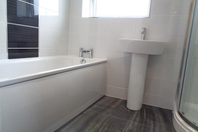 Mid-sized contemporary kids bathroom in West Midlands with a corner shower, a two-piece toilet, white tile, ceramic tile, white walls, porcelain floors, a pedestal sink, black floor and a sliding shower screen.
