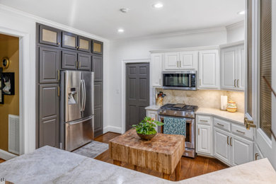 Example of a mid-sized classic u-shaped medium tone wood floor and brown floor enclosed kitchen design in Atlanta with an undermount sink, raised-panel cabinets, white cabinets, quartzite countertops, beige backsplash, stone slab backsplash, stainless steel appliances and beige countertops