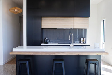 Mid-sized contemporary single-wall open plan kitchen in Melbourne with black cabinets, quartz benchtops, grey splashback, glass sheet splashback, black appliances, concrete floors, with island, flat-panel cabinets and a double-bowl sink.