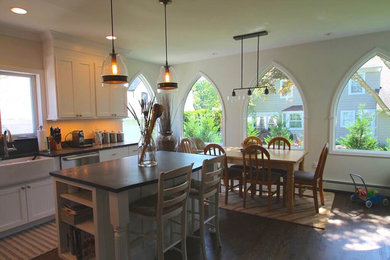 Example of a mid-sized classic u-shaped dark wood floor and brown floor eat-in kitchen design in New York with a farmhouse sink, shaker cabinets, white cabinets, soapstone countertops, white backsplash, stainless steel appliances, an island and black countertops