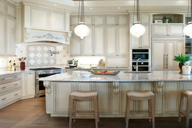 Large elegant l-shaped medium tone wood floor and brown floor kitchen photo in Portland with an undermount sink, raised-panel cabinets, beige cabinets, granite countertops, multicolored backsplash, ceramic backsplash, stainless steel appliances and an island