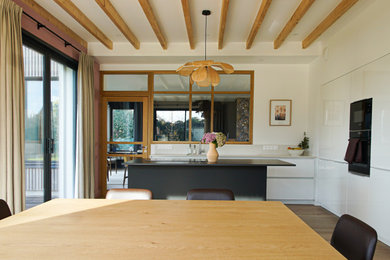 Idée de décoration pour une grande cuisine américaine parallèle et beige et blanche design avec un évier encastré, un placard avec porte à panneau encastré, des portes de placard blanches, un plan de travail en stratifié, une crédence beige, une crédence en céramique, parquet clair, îlot et un plan de travail beige.