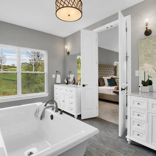 Cette photo montre une salle de bain principale nature avec une baignoire indépendante, des carreaux de céramique, un mur multicolore, un sol en carrelage de céramique, un plan de toilette en granite, un placard à porte persienne, des portes de placard blanches, un lavabo encastré et un sol gris.