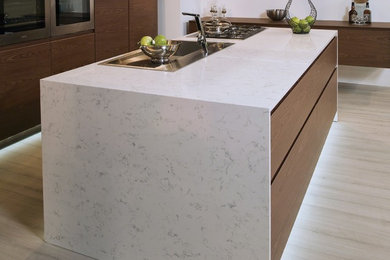 Mid-sized trendy l-shaped light wood floor and beige floor eat-in kitchen photo in Portland with a drop-in sink, flat-panel cabinets, dark wood cabinets, quartz countertops, stainless steel appliances and an island