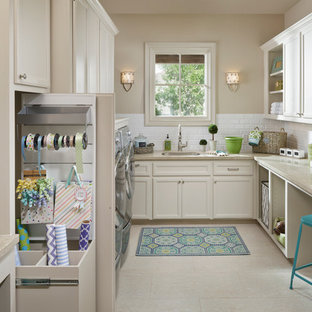 ヒューストンの大きいトラディショナルスタイルのおしゃれな家事室 (シングルシンク、落し込みパネル扉のキャビネット、白いキャビネット、ライムストーンカウンター、磁器タイルの床、左右配置の洗濯機・乾燥機、ベージュの壁、ベージュのキッチンカウンター) の写真