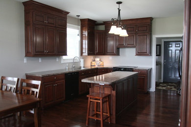 Example of a classic l-shaped eat-in kitchen design in Kansas City with an undermount sink, raised-panel cabinets, dark wood cabinets, laminate countertops and black appliances