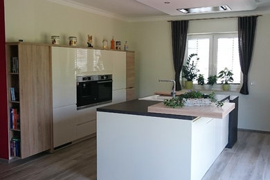 Offene, Große Moderne Küche mit Einbauwaschbecken, flächenbündigen Schrankfronten, gelben Schränken, Laminat-Arbeitsplatte, Küchengeräten aus Edelstahl, Keramikboden, Kücheninsel, braunem Boden und schwarzer Arbeitsplatte in Berlin
