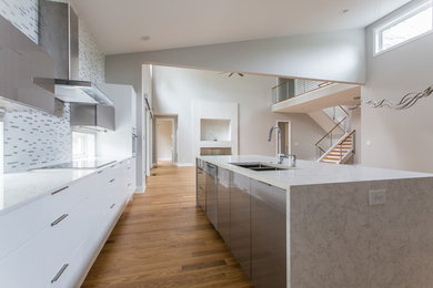 This is an example of a large contemporary l-shaped eat-in kitchen in Atlanta with an undermount sink, flat-panel cabinets, white cabinets, quartz benchtops, white splashback, mosaic tile splashback, white appliances, light hardwood floors, with island and beige floor.