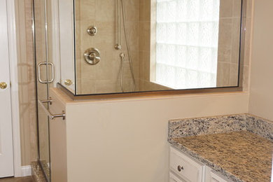 Photo of a mid-sized traditional master bathroom in Cincinnati with white cabinets, a corner shower, beige tile, granite benchtops, raised-panel cabinets, brown walls and an undermount sink.