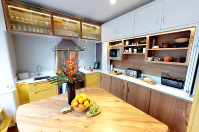 Photo of a large retro l-shaped kitchen/diner in Manchester with an integrated sink, flat-panel cabinets, yellow cabinets, engineered stone countertops, stainless steel appliances, porcelain flooring, an island and brown floors.